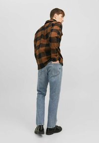 Camisa de franela a cuadros marrón y negra, de textura suave, corte relajado. Jeans azul claro, de pierna recta, de lavado claro. Zapatos negros.