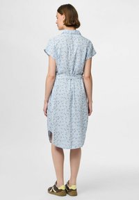 Ljusblå klänning med korta ärmar, blommönster, knytning i midjan och sidoklaffar. Tyget verkar mjukt och lätt.