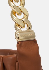 Tracolla in pelle marrone con un grande accento a catena dorata e una placca del marchio dorata con la scritta "MICHAEL KORS" incisa.