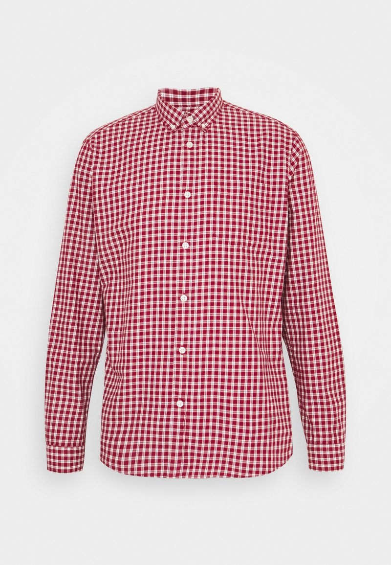 Chemise à carreaux rouge et blanche à manches longues, boutonnée, avec col et poche poitrine sur fond uni.