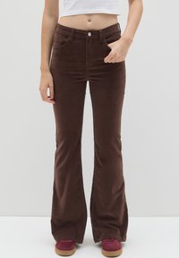 Bruine fluwelen wijde broek met een gladde textuur, hoge taille, voorzakken en een metalen knoopsluiting, gecombineerd met bordeauxkleurige schoenen.