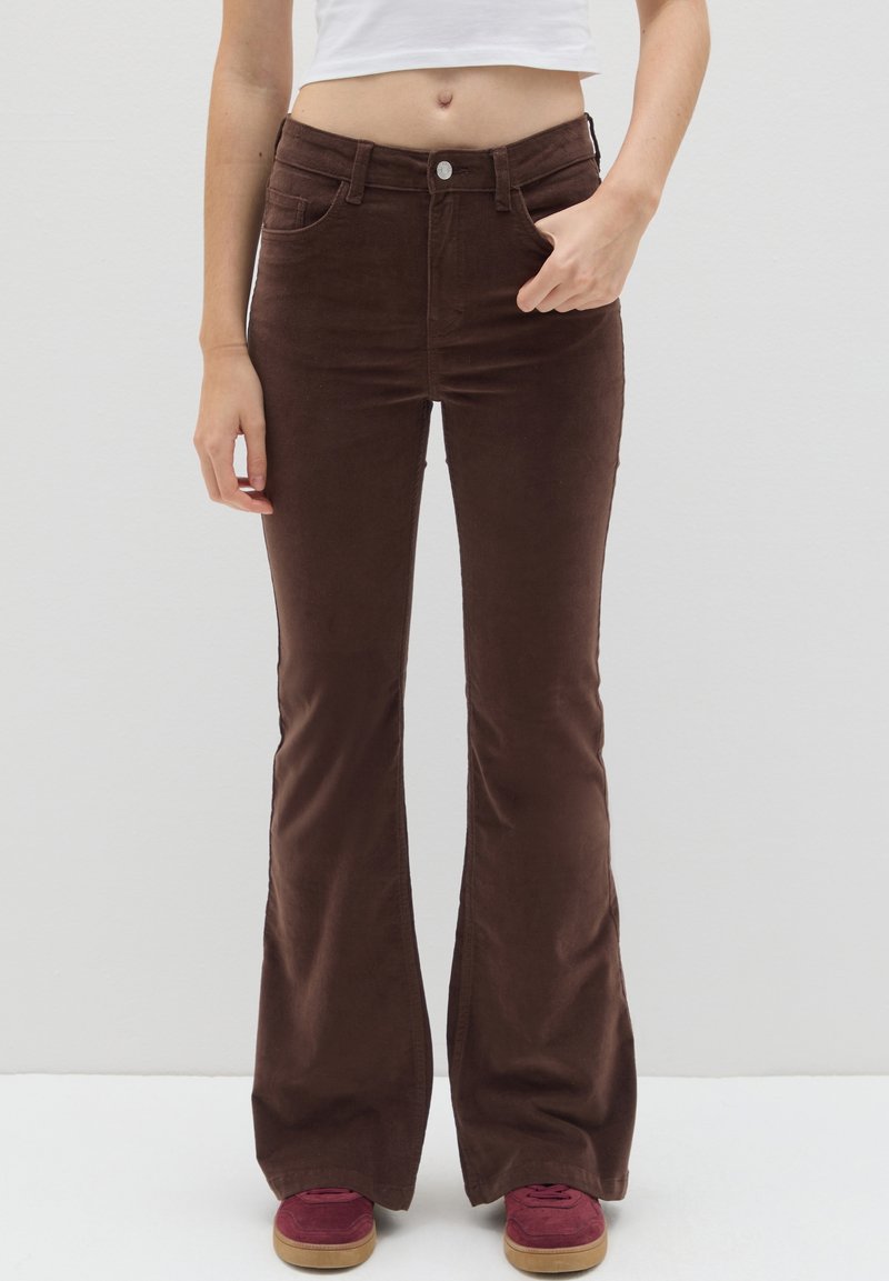 Bruine fluwelen wijde broek met een gladde textuur, hoge taille, voorzakken en een metalen knoopsluiting, gecombineerd met bordeauxkleurige schoenen.