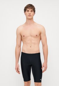 Čierne plavecké šortky vyrobené z elastického materiálu, s dĺžkou po kolená a priliehavým strihom. Na dolnej ľavej strane sa nachádza malé biele logo Nike.