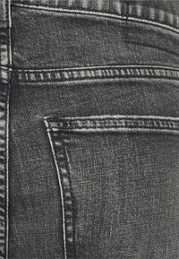 Jeans de denim cinza escuro com um design clássico de cinco bolsos, apresentando costuras visíveis e uma textura ligeiramente desbotada na área do bolso traseiro.