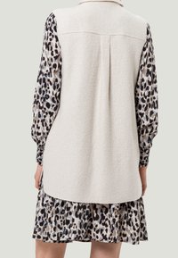 Beige Wollmischung ärmellose Weste mit Kragen, kombiniert mit einem langärmeligen Kleid im Tiermuster mit elastischen Bündchen und rüschenverziertem Saum.