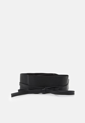 Large ceinture en cuir noir pliée avec une sangle étroite nouée en un nœud simple sur fond blanc.