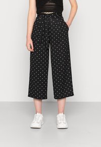 Svarta culotter med vita prickar, med knytmidja, sidofickor och vida ben. Bärs med vita sneakers. Slät tygtextur.