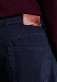 Tumedates teksased pruunist nahast plaastriga, millel on kiri "Pepe Jeans London" ja üks tagatasku.