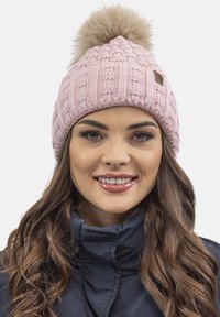 Berretto lavorato a maglia rosa con texture a coste, dotato di pompon in pelliccia sintetica sulla parte superiore e di un piccolo etichetta marrone sul lato.
