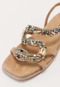 Beige semsket sandal med flat såle, dekorert med fargerike rhinestones og et slangeskåret metallisk accent på reima.