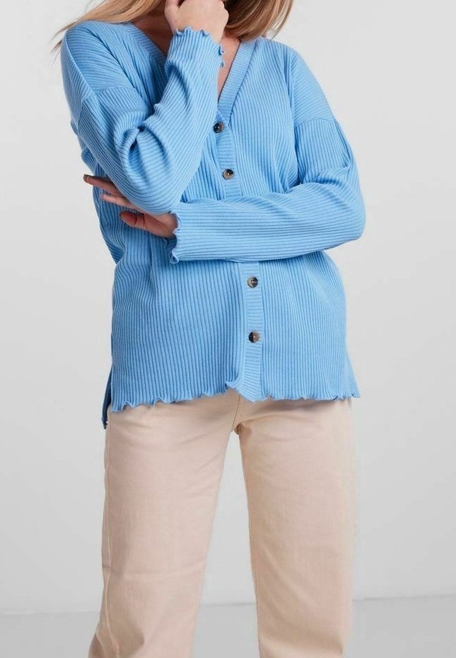 Ljusblå ribbad cardigan med knappstängning, V-ringning och vågig nederkant, i kombination med beiga raka byxor. Mjuk textur, avslappnad passform.