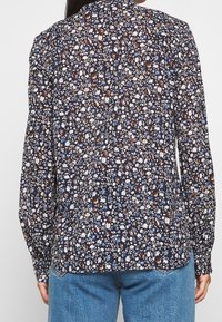 Blomsterbluse med en mørk navy baggrund, prydet med små hvide og farverige blomster mønstre. Lange ærmer og klassisk kravedesign.