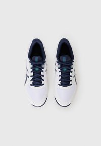 Baskets de sport blanches avec des accents bleu marine, des panneaux en maille et des lacets plats bleu marine. Elles présentent une semelle texturée et des détails de logo en vert.