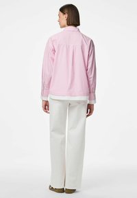 Camicia a righe rosa chiaro con colletto e polsini bianchi, abbinata a pantaloni bianchi a gamba larga. Pieghe posteriori visibili e polsini con bottoni.