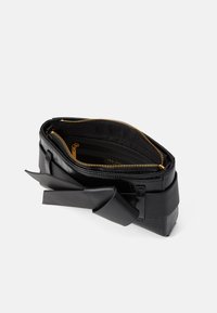 Bolsa de couro preto com textura em relevo de crocodilo, apresentando um fecho de zíper, bolsos interiores e um detalhe em couro amarrado na lateral.
