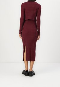 Bordový žebrovaný dvoudílný outfit s dlouhými rukávy, zkráceným topem a sukní střední délky s bočním rozparkem. Kombinováno s černými masivními botami.