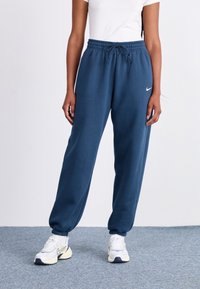 Pantalones deportivos azul marino con cintura elástica y cordón ajustable. Diseñados con piernas ajustadas y un pequeño logo blanco de Nike en el muslo izquierdo.