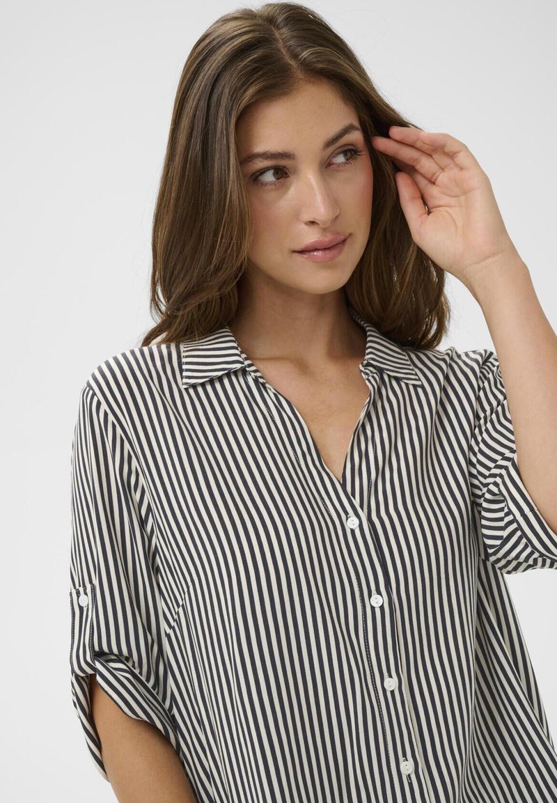 Loose-fitting button-up shirt with a collar, featuring vertical black and white stripes, short rolled sleeves, and smooth fabric texture.