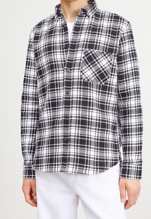 Camisa de cuadro en blanco y negro, con cuello puntiagudo, bolsillo frontal y mangas largas, hecha de una tela suave con un patrón a cuadros.
