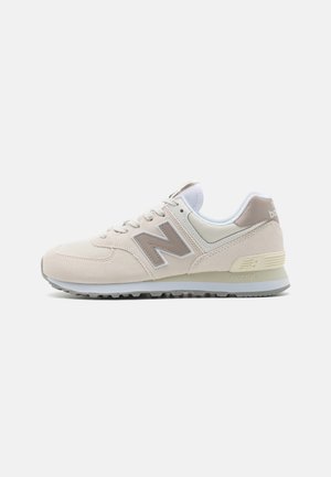 Beige Sportschuh mit Obermaterial aus Wildleder und Mesh, ausgestattet mit einem hellgrauen N-Logo, weißen Schnürsenkeln und einer strukturierten Gummisohle.
