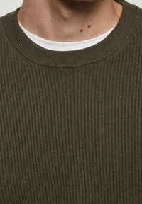 Maglione a coste verde oliva con scollatura rotonda e uno strato interno bianco a contrasto visibile al colletto. Dettaglio in tessuto testurizzato.