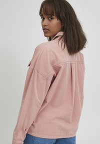 Roze langslipshirt van zacht materiaal, met een gekraagde halslijn, een relaxte pasvorm en gedetailleerd garen op de achterkant en mouwen.