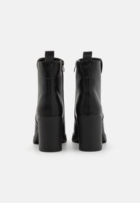 Stivaletti neri in pelle con finitura liscia, tacco a blocco e chiusura con zip sul retro. Linee pulite e design minimalista.