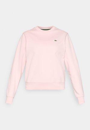 Lys rosa crewneck sweatshirt med lange ermer og en liten grønn krokodillelogo på venstre bryst, vist på hvit bakgrunn.