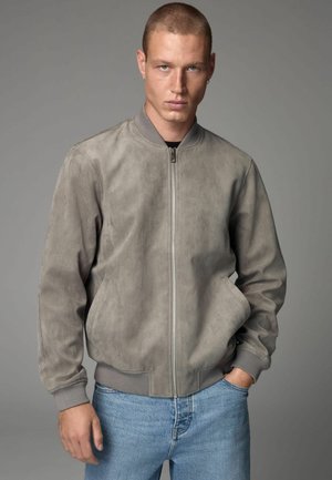 Gray suede bomber jacket with a front zipper, ribbed cuffs, and collar; paired with light blue denim jeans. Clean, minimal design.