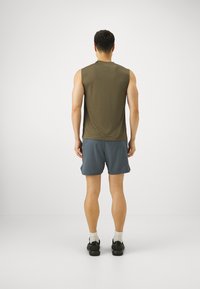 Olivegrön ärmlös topp, blå träningsshorts, kombinerad med svarta skor och vita strumpor, sedd bakifrån mot en neutral bakgrund.