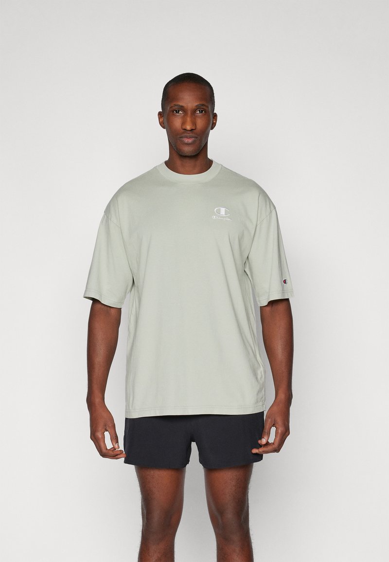 Lys grøn bomulds T-shirt med korte ærmer og rund hals, der har et lille logo på brystet. Bærende med mørke shorts.