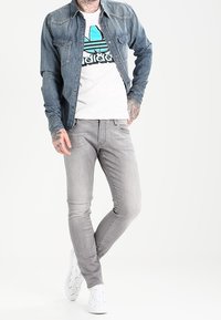 Jeansjacka i blått, figurnära vit t-shirt med turkos grafik, grå smal passform jeans och vita sneakers med texturerad design.