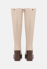 Knee-high beige boots with side zippers and a textured brown block heel. Smooth leather-like material with minimalistic design and subtle hardware accents.