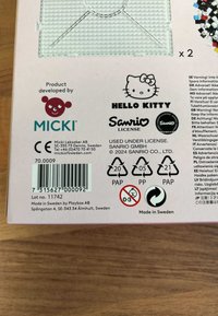 MICKI Hello Kitty tuotekäärintä, vaaleanpunainen tausta, sisältää brändilogot, viivakoodin, kierrätyssymbolit ja turvallisuusvaroitukset ikäryhmälle 0-3.