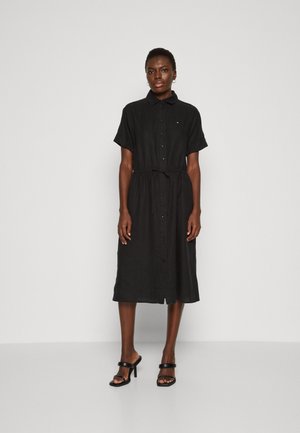 Abito camicia nero con bottoni, maniche corte, vita aderente e orlo a ginocchio. Tessuto liscio e sottile loghetto in prossimità del colletto.