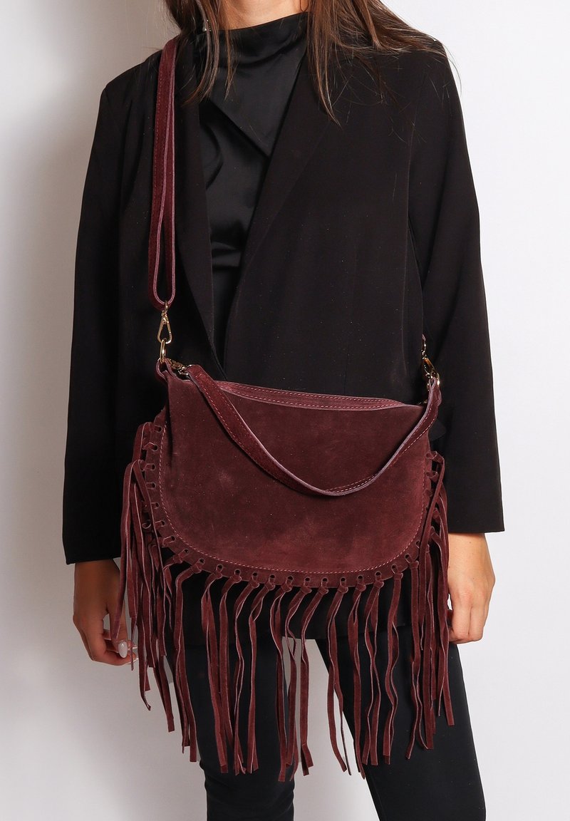 Borsa a tracolla in suede bordeaux con frange sulla parte inferiore, dotata di una patta curvata e hardware dorato. Cinghia regolabile per versatilità.