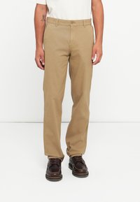 Beige canvas trousers with a straight-leg design, front pockets, and a button closure. Paired with brown lace-up shoes.