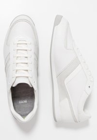 Bílé tenisky s koženými a semišovými akcenty, kulatou špičkou, plochým šněrováním a texturovanou stélkou, s jednoduchým, čistým designem.