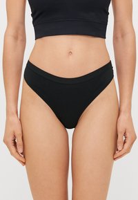 Svart bomulls-bikini med mid-rise design. Har en glatt midjebånd og minimal dekning på sidene. Myk, elastisk tekstur.