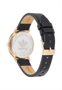 Auksinis nerūdijančio plieno laikrodis su juodu odiniu dirželiu. Apvalus ciferblatas, minimalistiškas dizainas, su "Adidas" logotipu ir lygia apdaila.