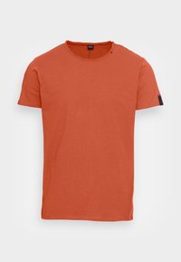 Camiseta naranja quemado hecha de algodón suave, con cuello redondo y mangas cortas. Diseño liso con un pequeño logo en la manga.
