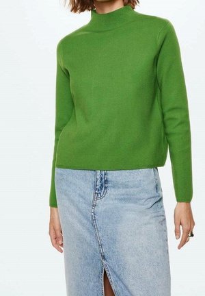 Femme portant un pull vert vif à manches longues et une jupe en denim bleu clair taille haute avec une fente à l'avant.