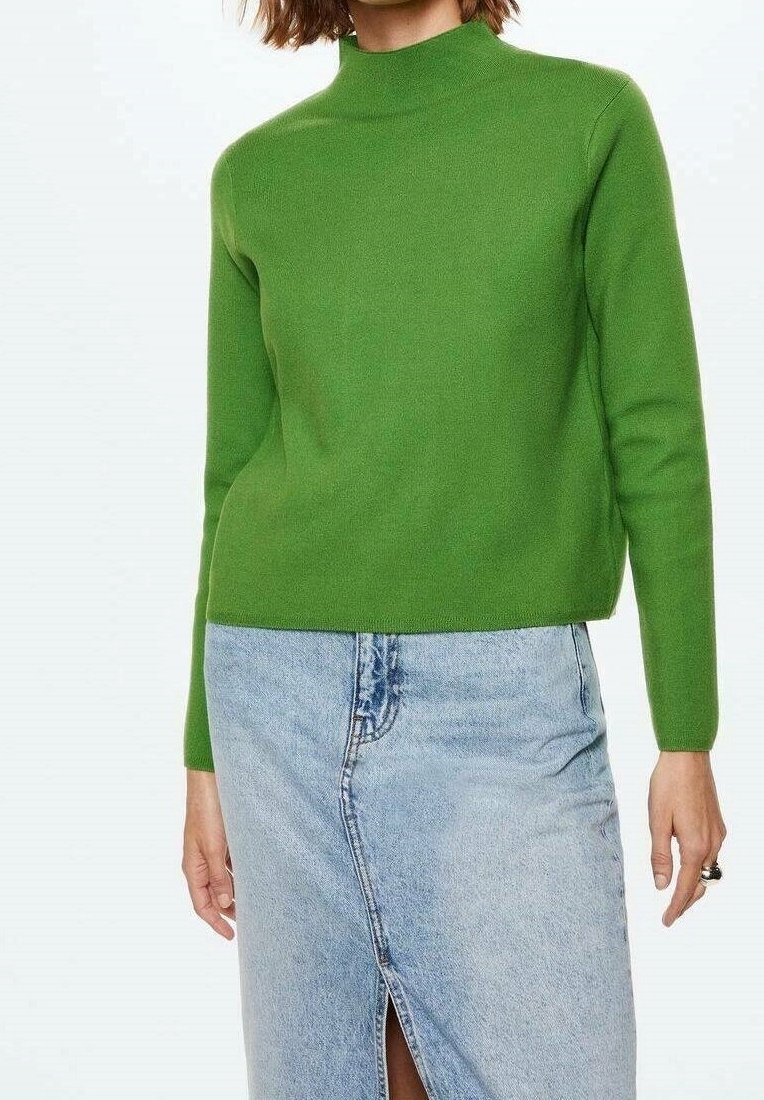 Femme portant un pull vert vif à manches longues et une jupe en denim bleu clair taille haute avec une fente à l'avant.