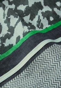 Écharpe ornée d'un mélange de motifs graphiques : formes abstraites en gris et blanc, bordée de vert et terminée par un bord en chevrons.
