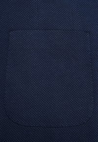 Granatowy materiał z subtelnym wzorem diamentowym; posiada zakrzywioną kieszeń z przeszytymi brzegami, tworzącą teksturowany wzór.