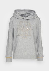 Grijze hoodie met een ruime capuchon, voorzien van een decoratief logo-ontwerp met gouden accenten en textuurmanchetten. Gemaakt van zachte stof voor comfort.