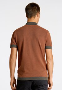 Brun stickad polotröja med korta ärmar, med en kontrasterande grön krage och ärmslut. Texturerad tyg, avslappnad passform och sidoklistermärke.