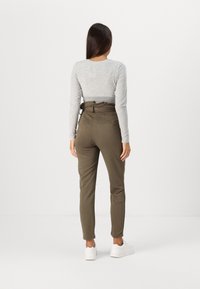 Haut gris à manches longues et pantalon taille haute vert olive avec une taille à volants, doté de deux poches arrière. Porté avec des baskets blanches.