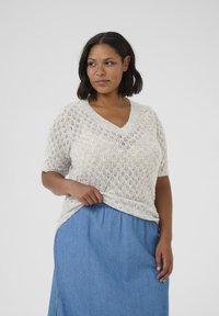 Hellgrauer, kurzärmeliger Strickpullover mit V-Ausschnitt und Rautenmuster, kombiniert mit einem blauen Jeansrock.