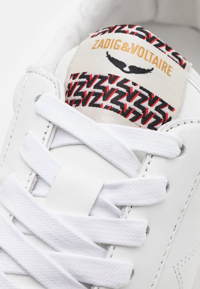 Fehér bőr sneaker lapos fehér fűzőkkel, piros és fekete mintás talpbéléssel, aranybetűs "ZADIG&VOLTAIRE" felirattal.
